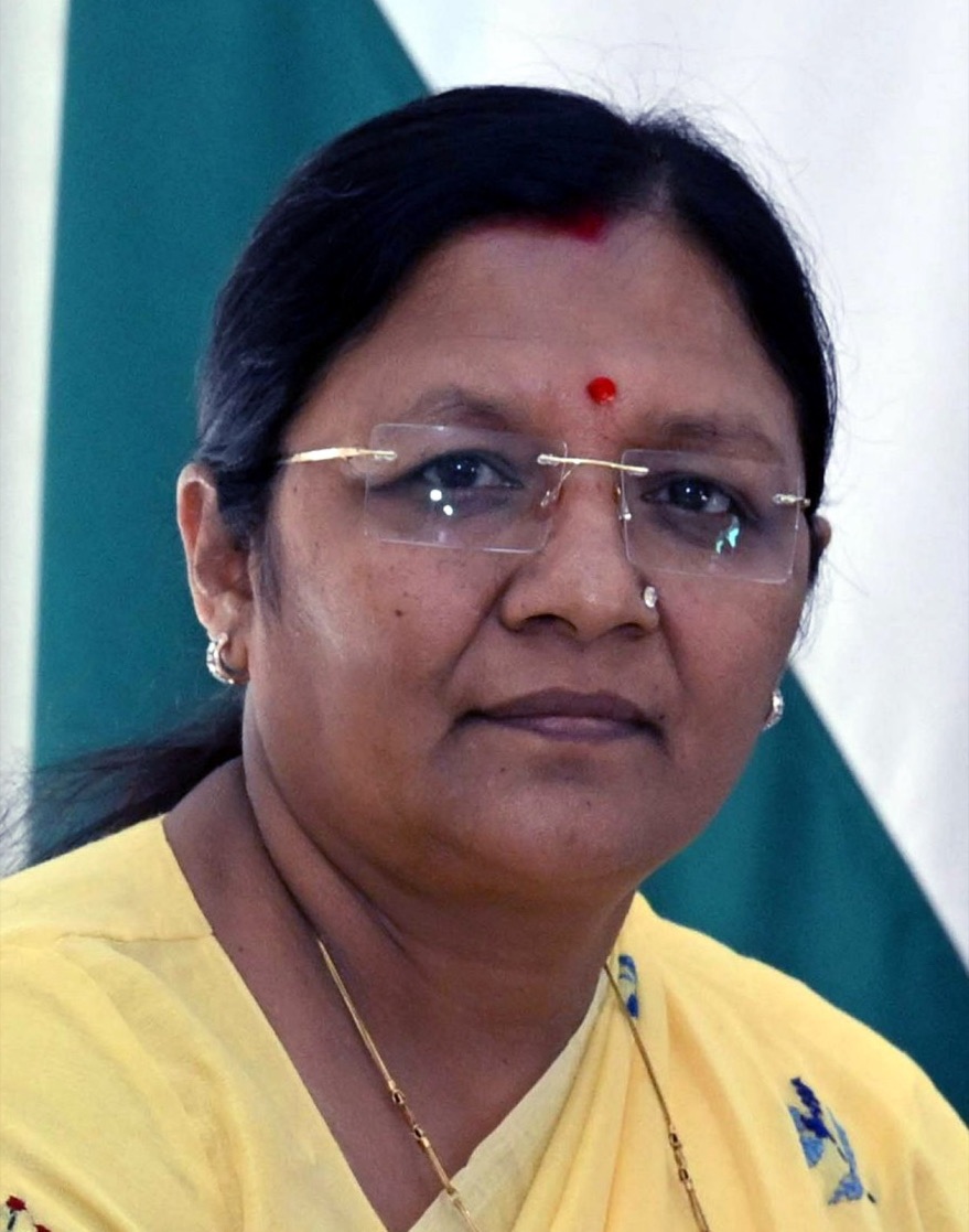 Official portrait of Smt. Savitri Thakur in a yellow sari, with a flag behind her.