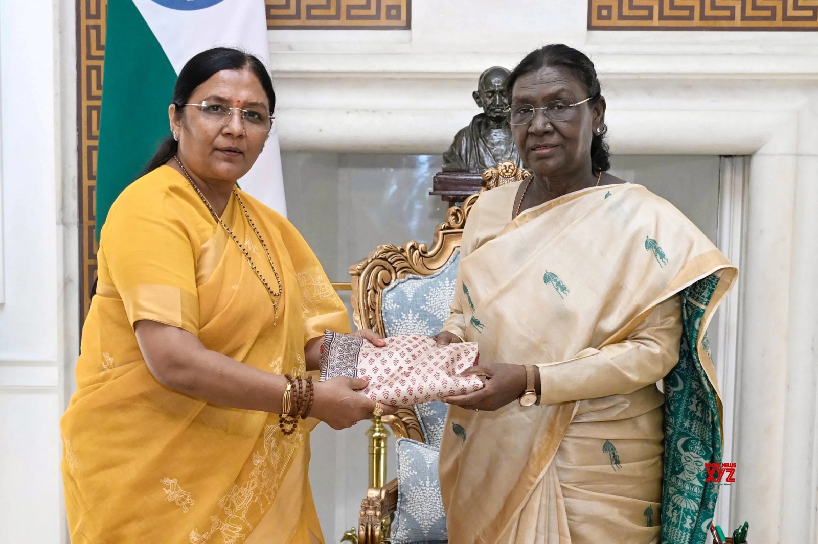 Smt. Savitri Thakur presenting a folded handloom textile to the President of India, Smt. Droupadi Murmu.