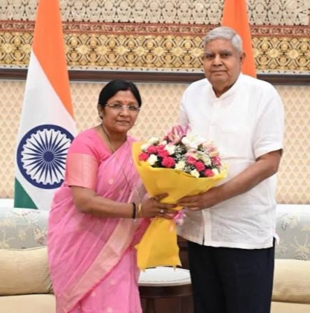 Smt. Savitri Thakur presenting a bouquet to the Vice-President of India, with the National Flag behind.