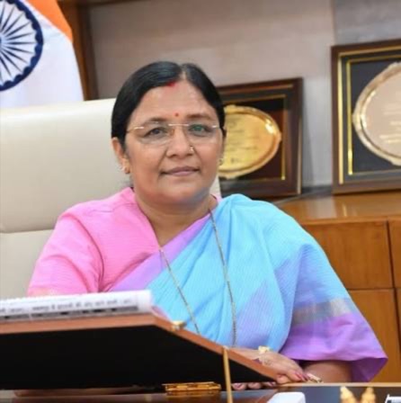Smt. Savitri Thakur seated at an official desk with the National Flag of India beside her.